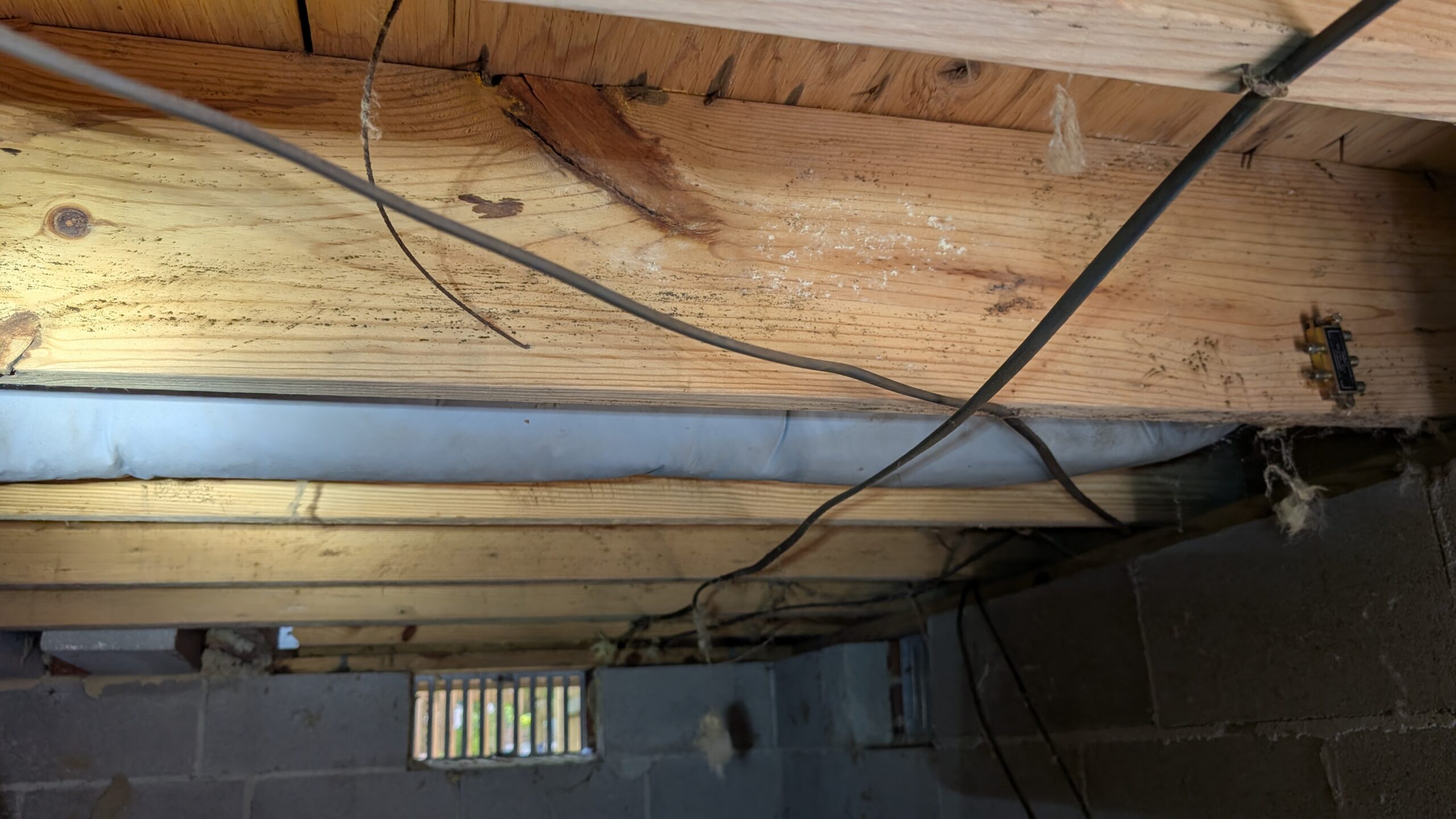 Exposed ceiling joists, electrical wires, and ductwork in an unfinished basement with cinder block walls and a small window.